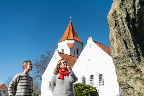 Line Modin og Mette Geil foran den dannebrogsfarvede frimenighedskirke ved mindestenen for de 16 unge mænd fra menigheden, der faldt i 1. Verdenskrigs skyttegrave i blandt andet Rusland og Frankrig. Foto: Palle Peter Skov 